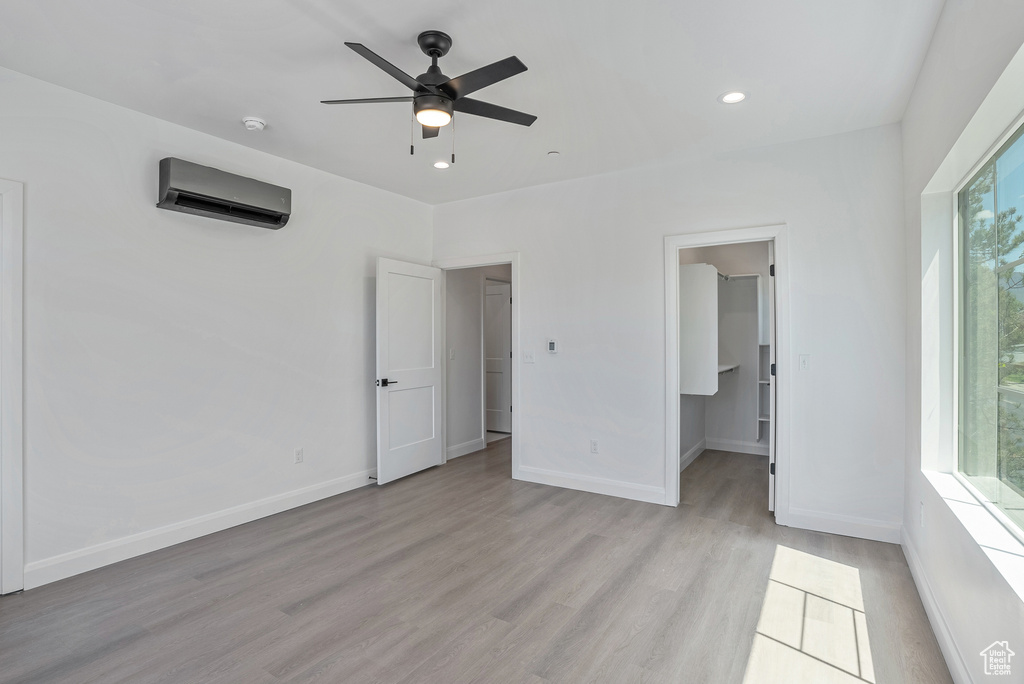 Empty room featuring an AC wall unit, light wood-style flooring, a ceiling fan, baseboards, and recessed lighting