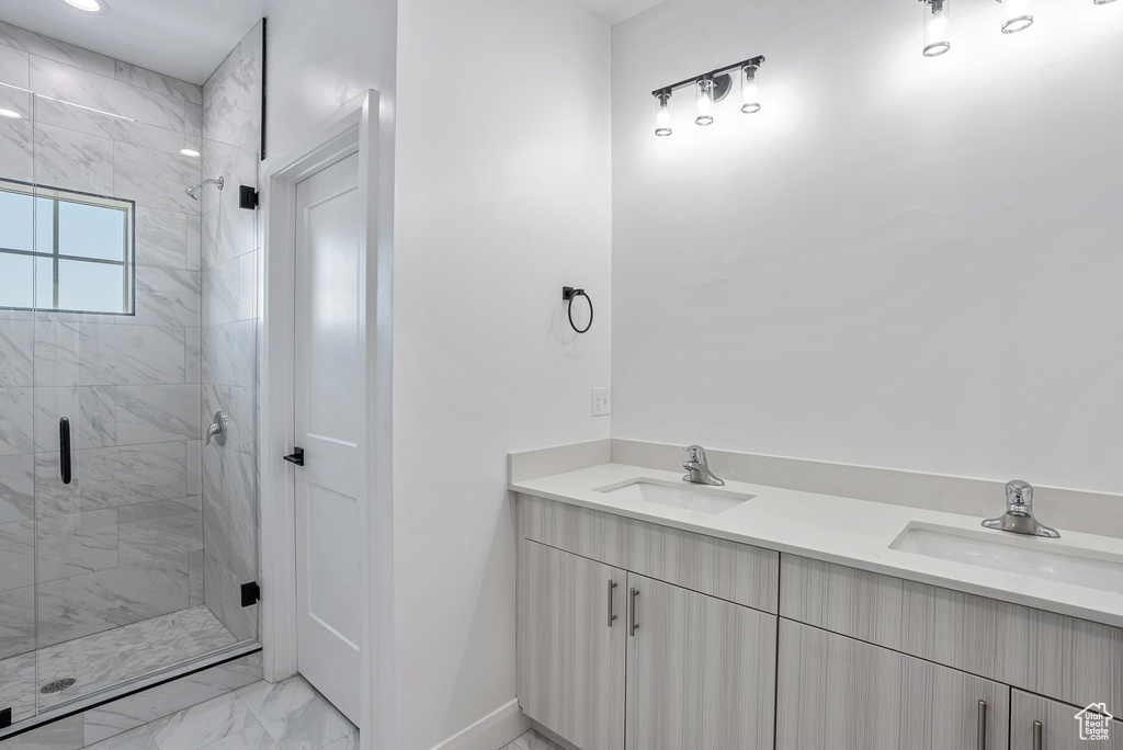 Full bath featuring marble look tiles, double vanity, a stall shower, and baseboards