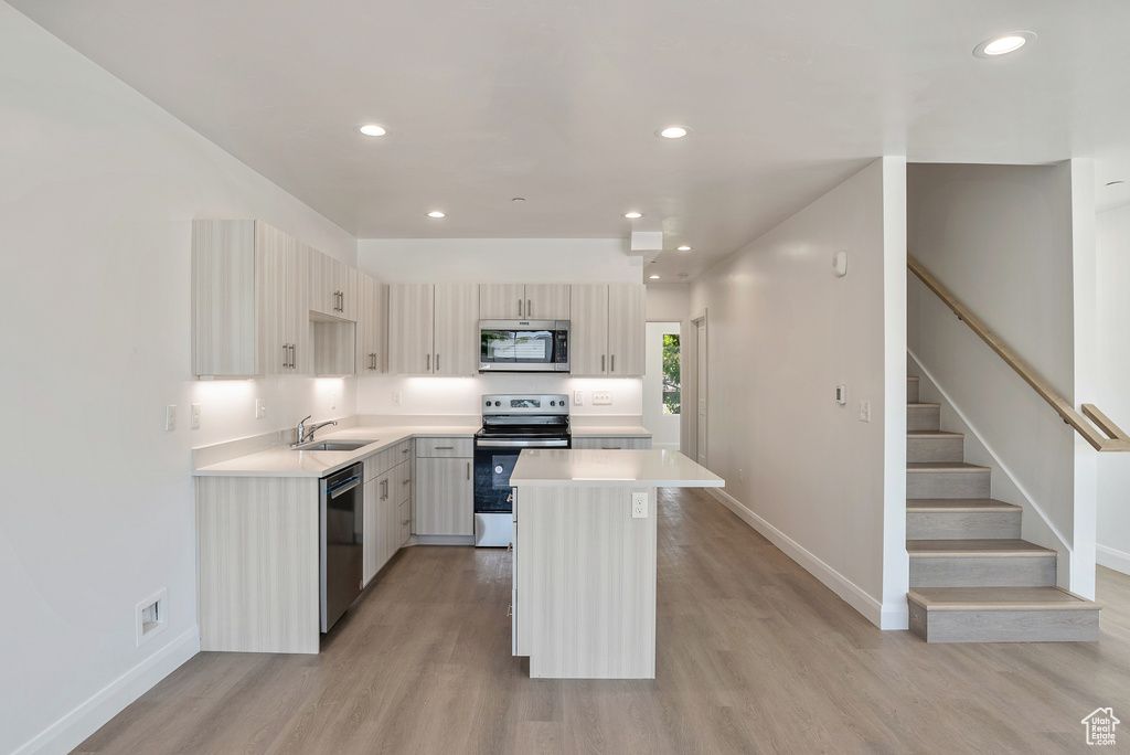 Kitchen featuring appliances with stainless steel finishes, a sink, baseboards, light wood finished floors, and light countertops