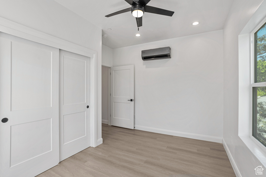 Unfurnished bedroom featuring a wall mounted air conditioner, baseboards, light wood finished floors, recessed lighting, and a closet