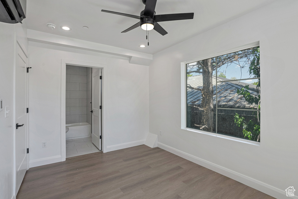 Unfurnished bedroom featuring baseboards, recessed lighting, wood finished floors, connected bathroom, and an AC wall unit