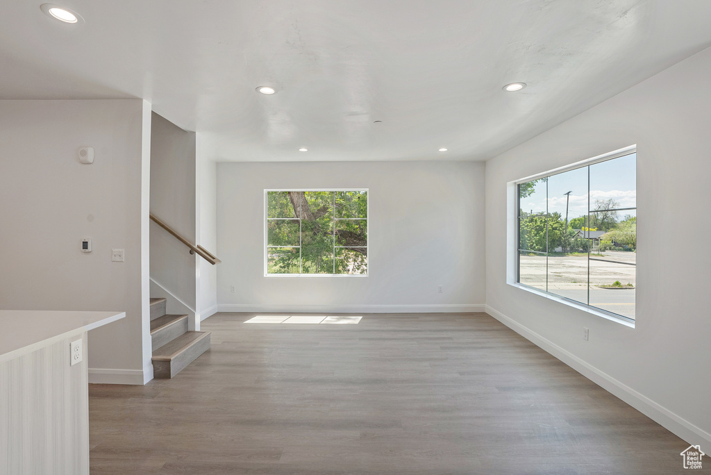Unfurnished room featuring healthy amount of natural light, recessed lighting, baseboards, stairway, and light wood-style floors