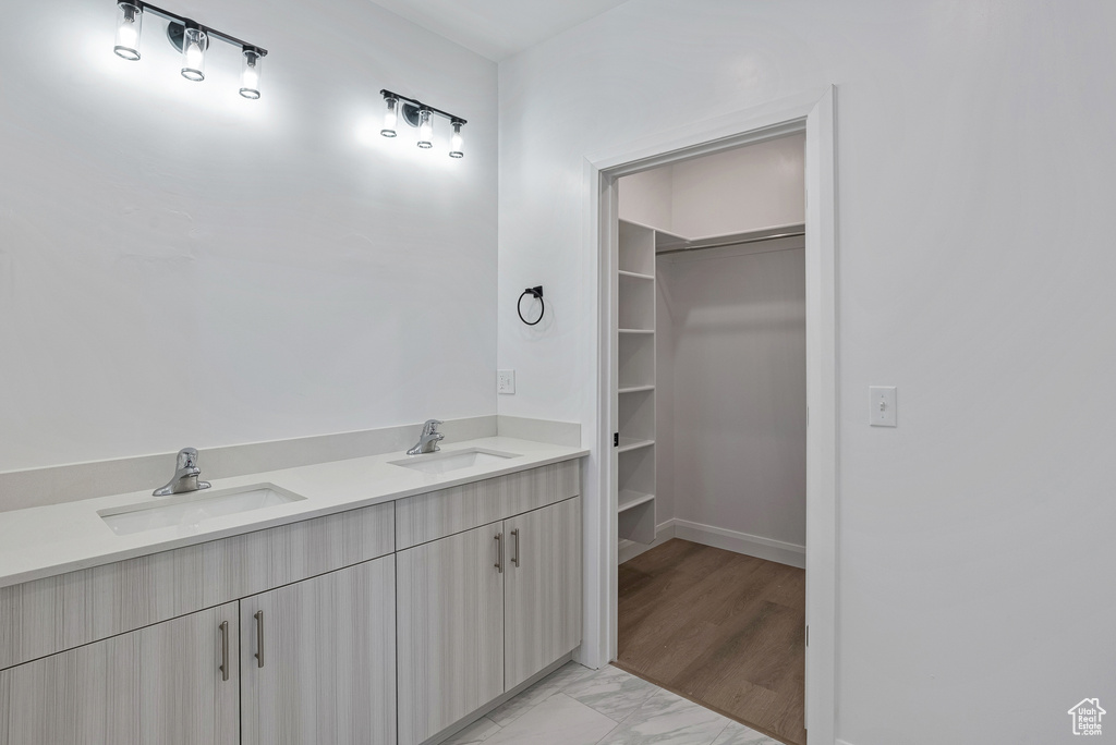Full bath featuring a spacious closet, double vanity, marble look tiles, and baseboards