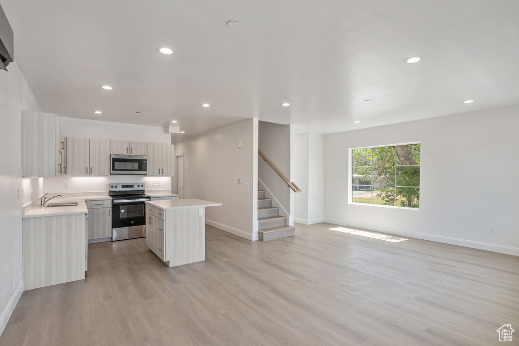 Kitchen featuring appliances with stainless steel finishes, a sink, light countertops, a kitchen island, and baseboards