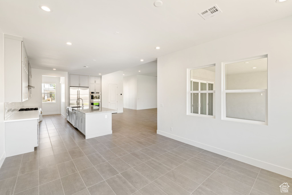 Kitchen with stainless steel appliances, light countertops, open floor plan, a center island with sink, and white cabinetry