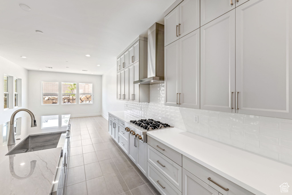Kitchen featuring stainless steel gas stovetop, wall chimney range hood, a sink, decorative backsplash, and light tile patterned floors
