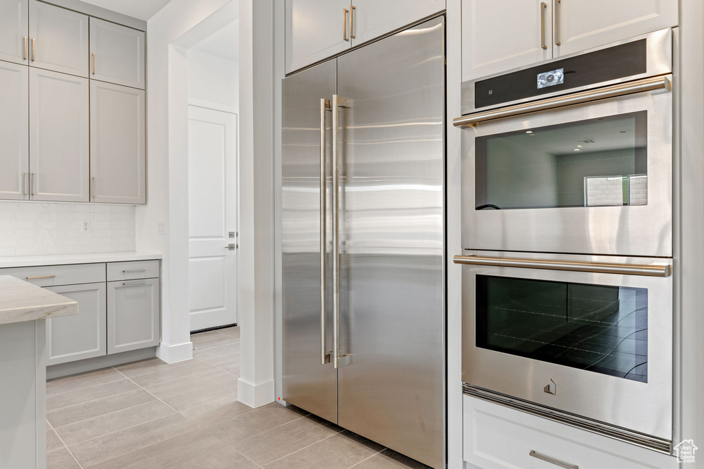 Kitchen featuring stainless steel appliances, light tile patterned flooring, light countertops, and tasteful backsplash