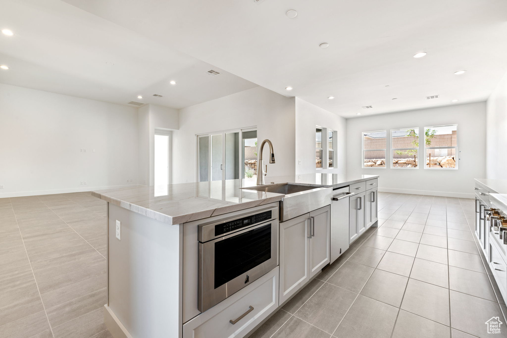 Kitchen featuring light tile patterned floors, a sink, a center island with sink, recessed lighting, and light stone counters