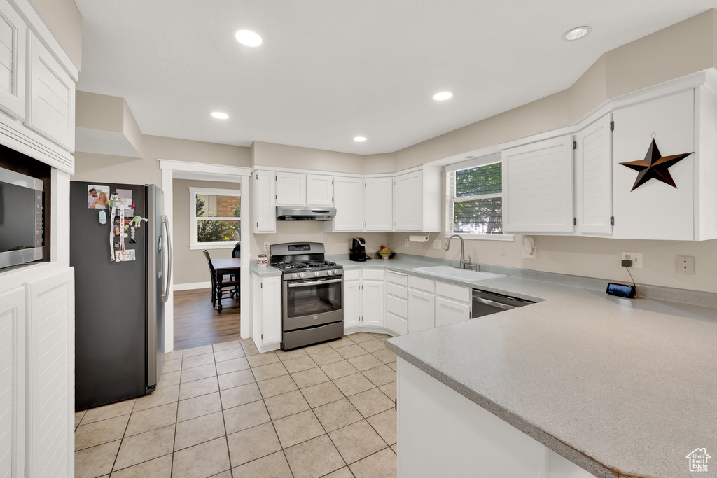 Kitchen with appliances with stainless steel finishes, under cabinet range hood, a sink, white cabinetry, and light countertops