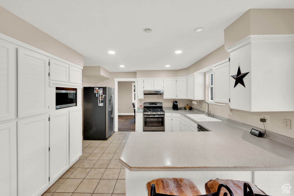 Kitchen featuring appliances with stainless steel finishes, under cabinet range hood, a sink, a peninsula, and light countertops