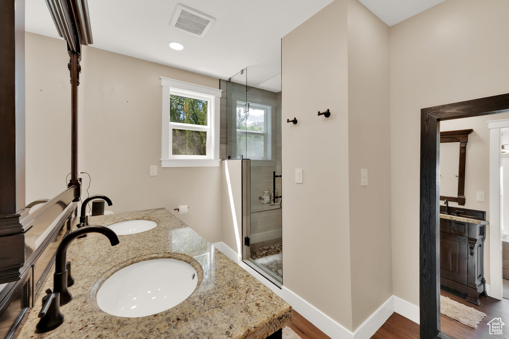 Full bathroom featuring double vanity, a shower stall, wood finished floors, baseboards, and recessed lighting