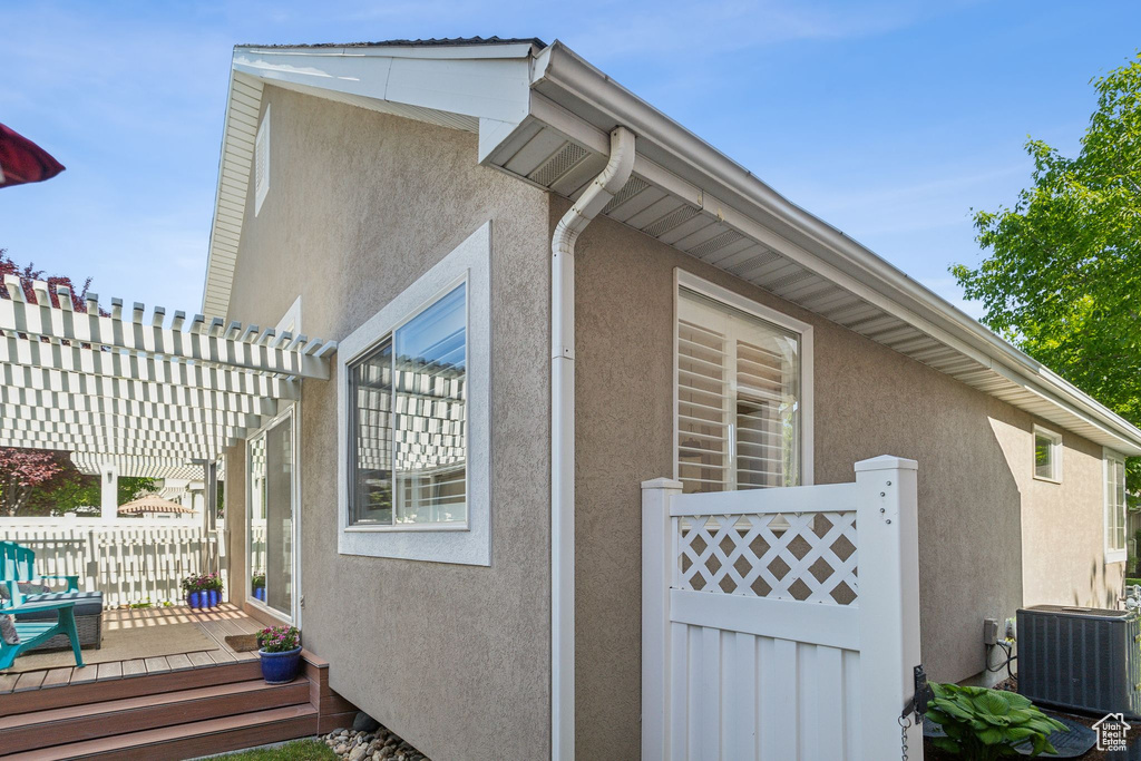 View of side of home with central AC, stucco siding, a deck, and a pergola