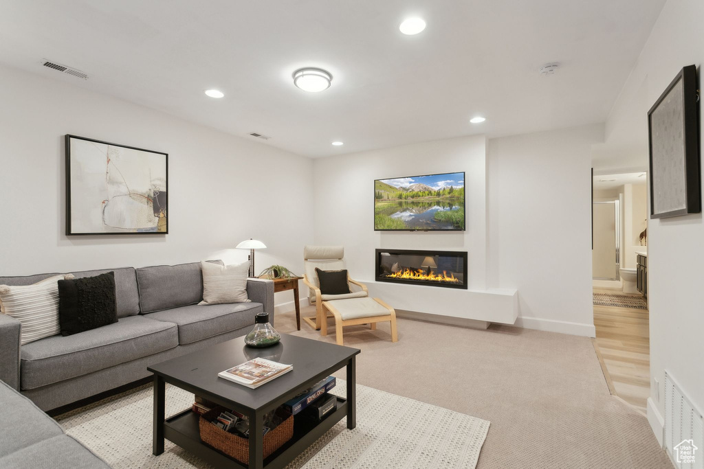 Living room featuring a glass covered fireplace, recessed lighting, light carpet, and baseboards