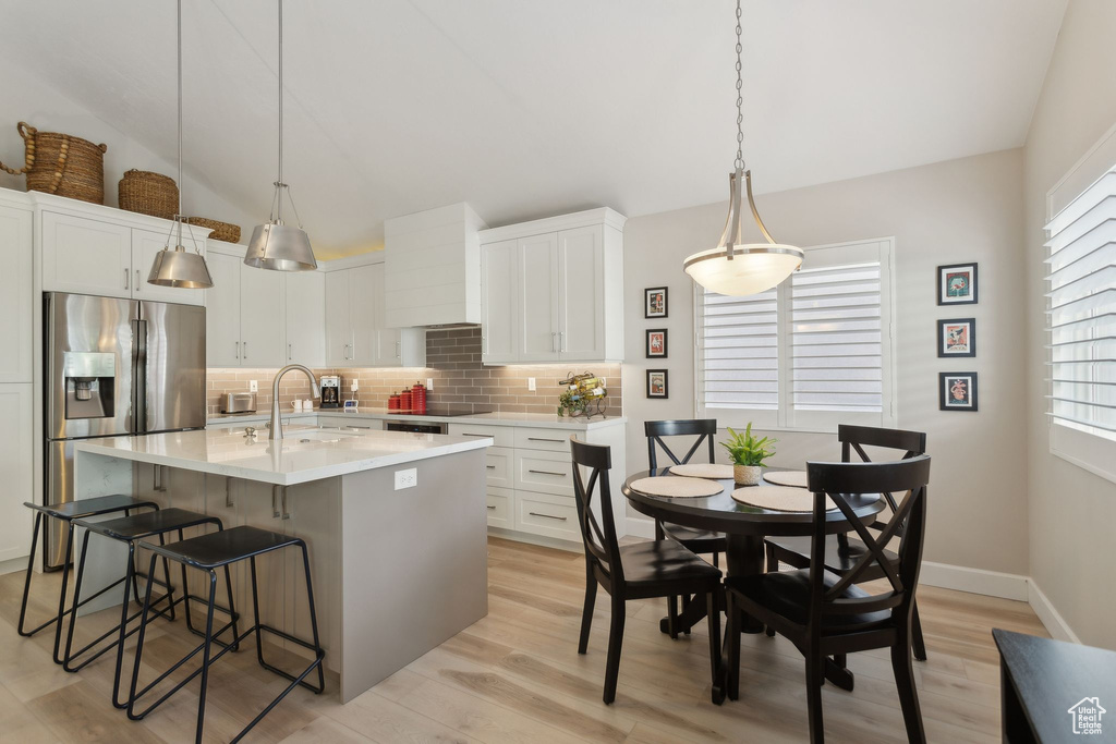 Kitchen with stainless steel fridge, a sink, a breakfast bar, backsplash, and white cabinetry