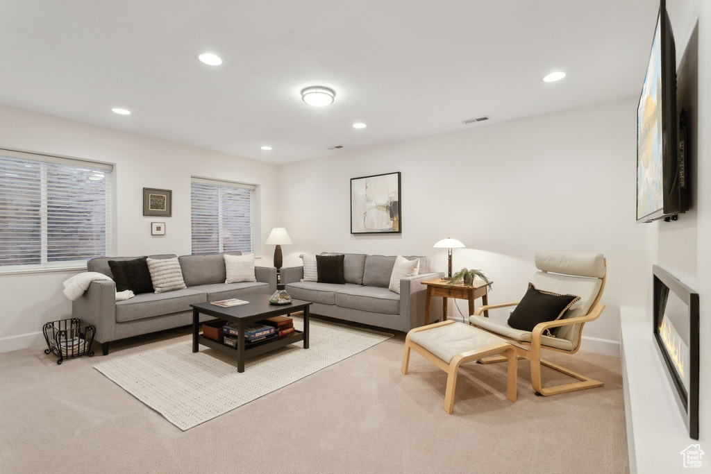 Living area with light colored carpet, baseboards, recessed lighting, and a glass covered fireplace