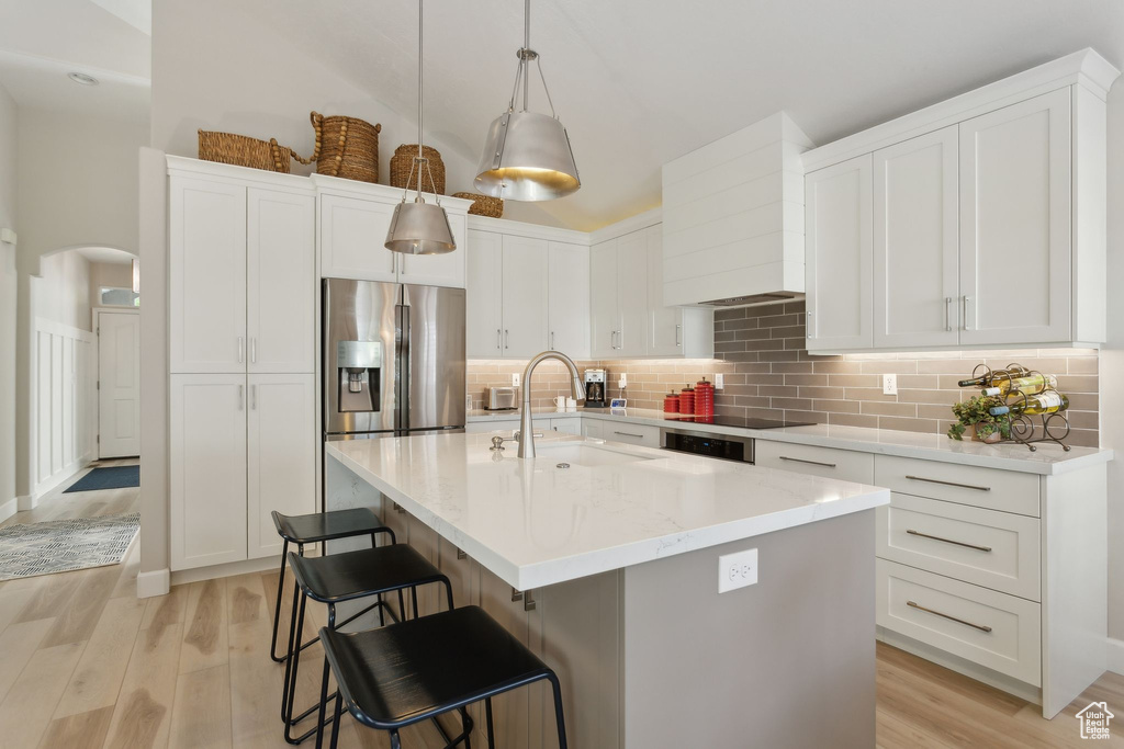 Kitchen featuring a sink, stainless steel fridge, arched walkways, light wood-style floors, and white cabinets