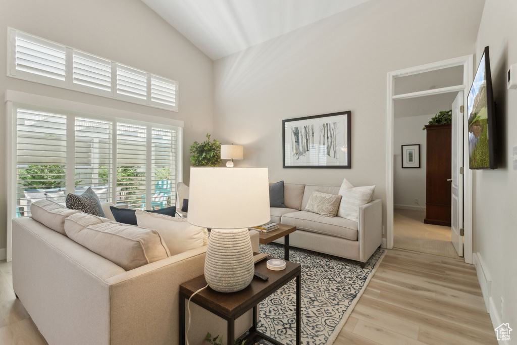 Living area with plenty of natural light, light wood-style floors, high vaulted ceiling, and baseboards