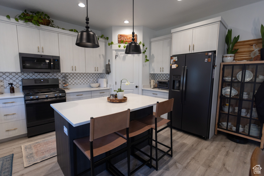 Kitchen with black appliances, a breakfast bar, light countertops, backsplash, and recessed lighting