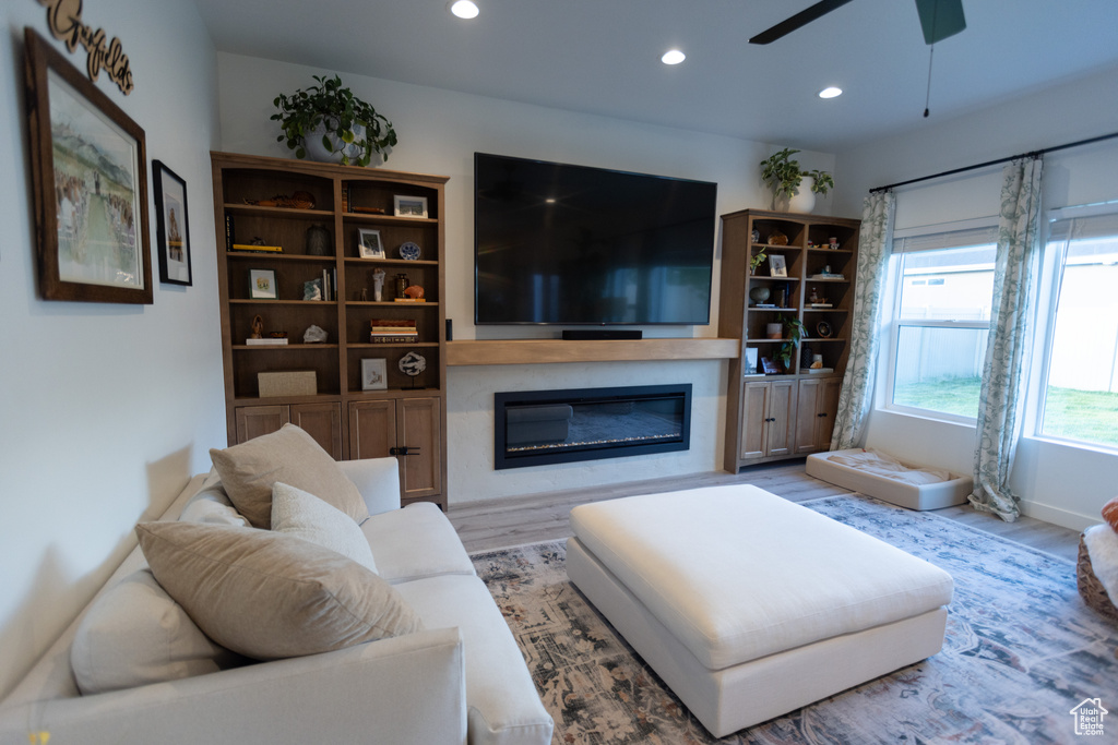 Living area with a glass covered fireplace, wood finished floors, recessed lighting, and ceiling fan
