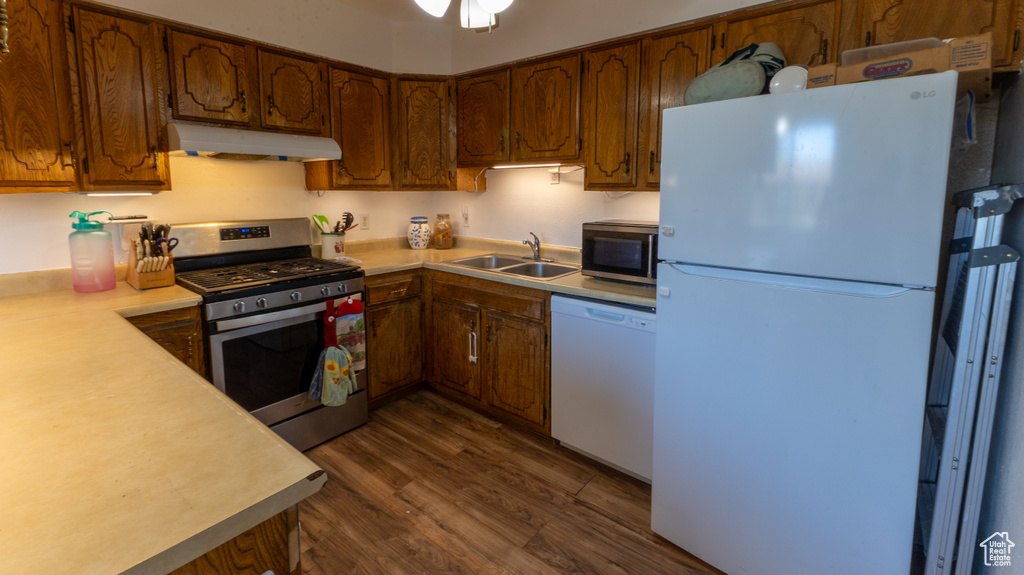 Kitchen with stainless steel appliances, under cabinet range hood, a sink, light countertops, and dark wood-style flooring