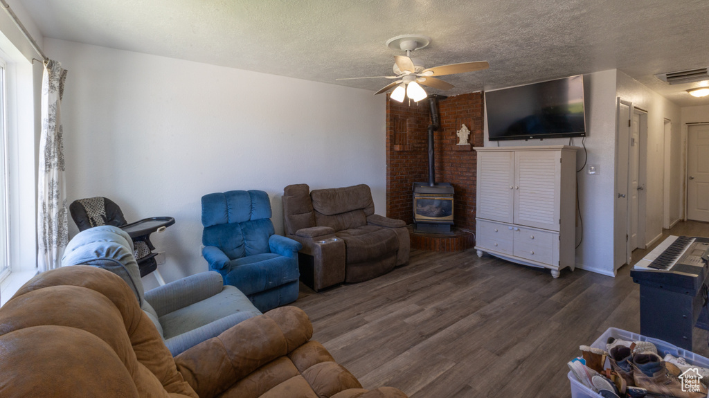 Living area with a wood stove, wood finished floors, ceiling fan, and a textured ceiling