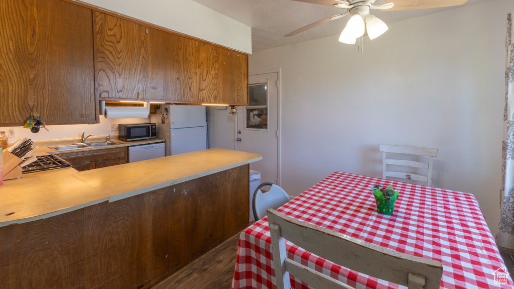 Kitchen with white appliances, a sink, a peninsula, dark wood-style flooring, and a ceiling fan