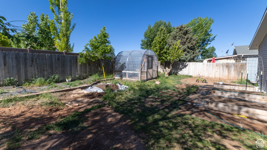 Fenced backyard featuring a greenhouse, a vegetable garden, and an outdoor structure