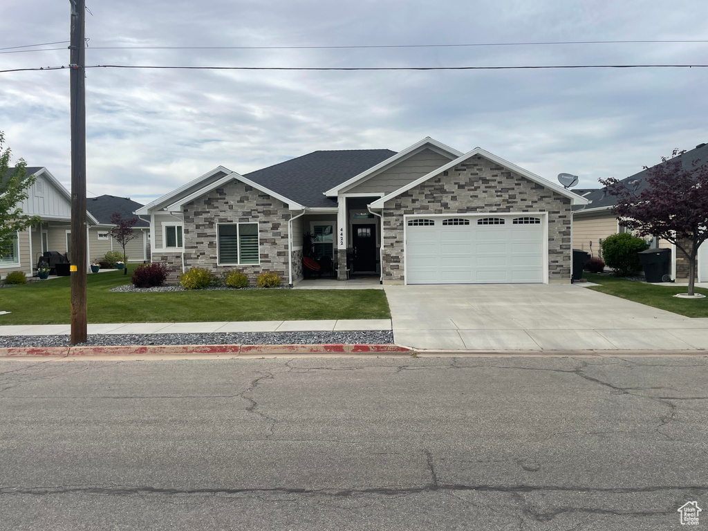 View of front facade featuring stone siding, a front lawn, driveway, and an attached garage
