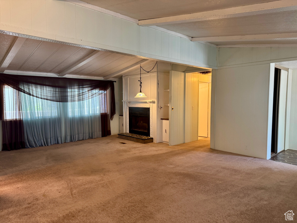 Unfurnished living room featuring beamed ceiling, carpet floors, and a fireplace with raised hearth