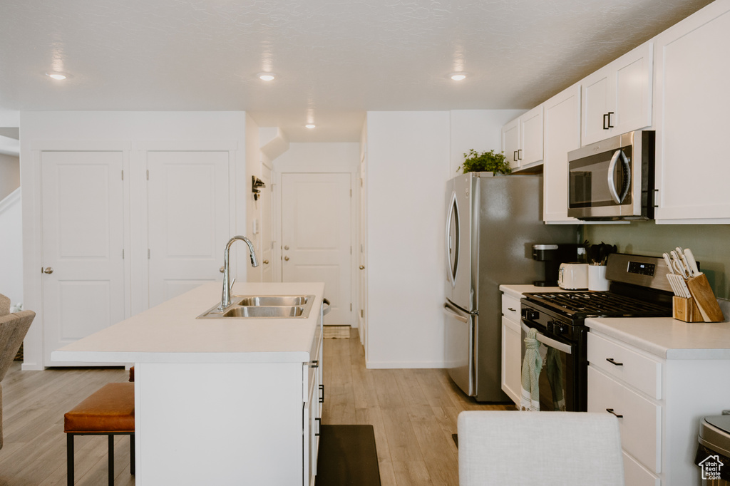 Kitchen featuring appliances with stainless steel finishes, a sink, light wood finished floors, a kitchen island with sink, and recessed lighting