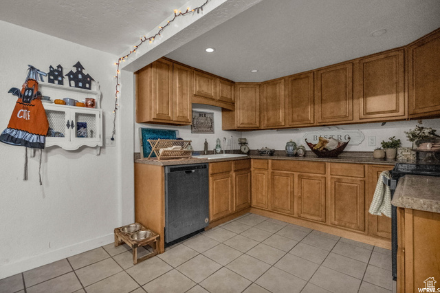 Kitchen featuring black dishwasher, a sink, brown cabinetry, light tile patterned floors, and baseboards