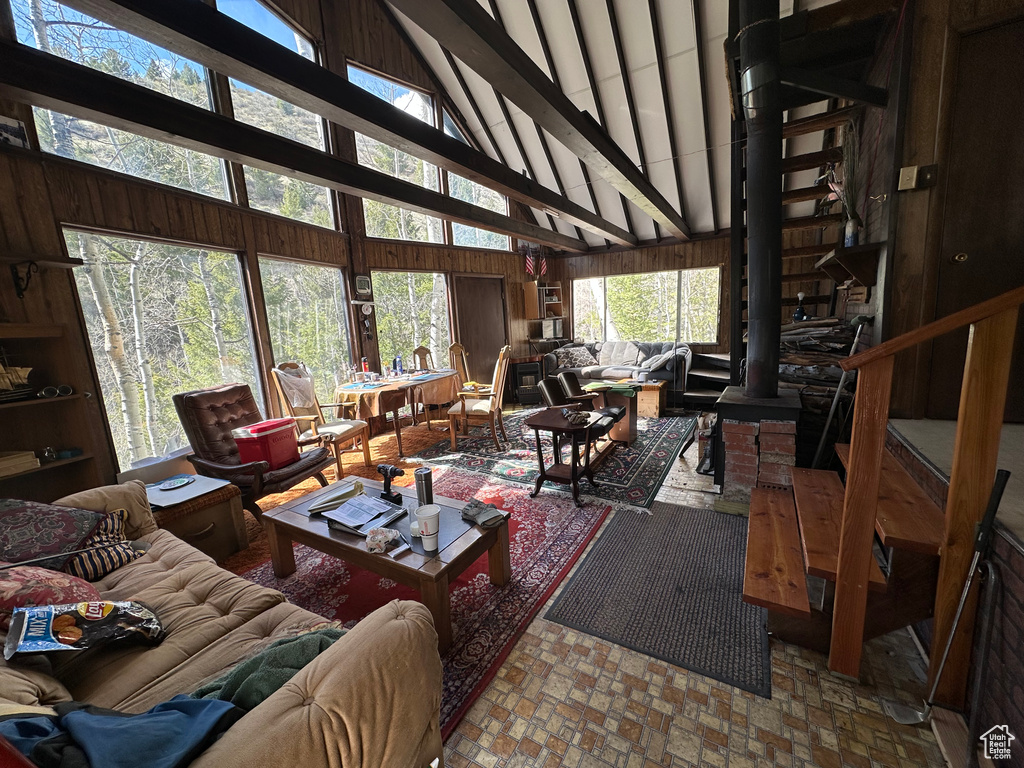 Living room featuring brick patterned flooring, beam ceiling, healthy amount of natural light, and wooden walls