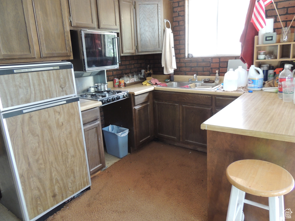 Kitchen featuring fridge, light countertops, carpet flooring, a sink, and a kitchen bar