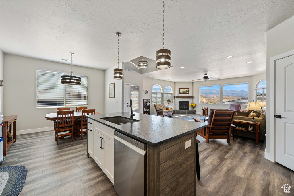 Kitchen featuring dishwasher, a sink, dark countertops, dark wood-style flooring, and baseboards