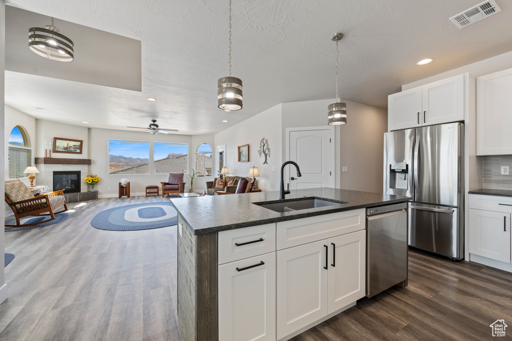 Kitchen with a sink, stainless steel appliances, dark wood finished floors, a glass covered fireplace, and a center island with sink