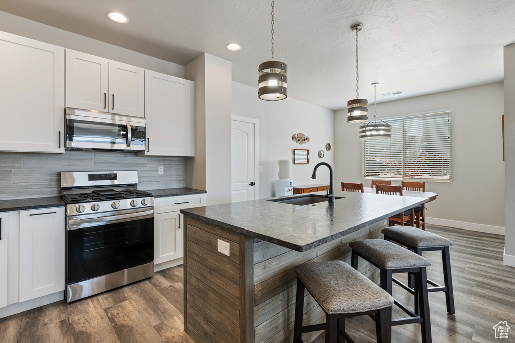 Kitchen with appliances with stainless steel finishes, a sink, backsplash, baseboards, and a kitchen bar