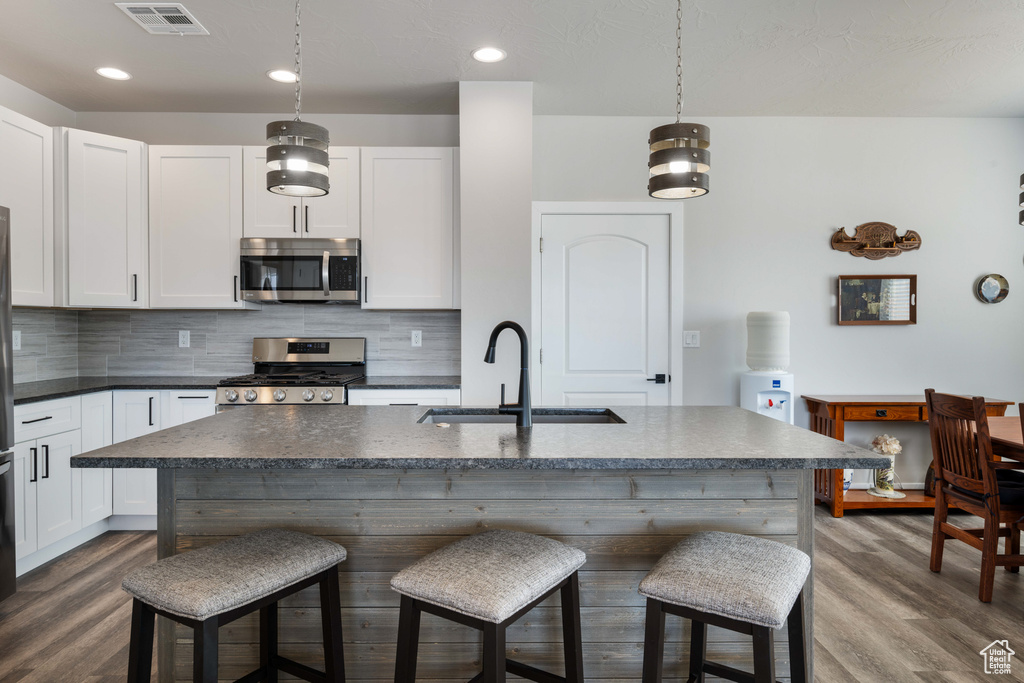 Kitchen featuring stainless steel appliances, a sink, dark countertops, dark wood finished floors, and recessed lighting