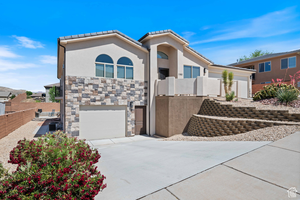 View of front of property with driveway, stucco siding, an attached garage, stone siding, and a tiled roof