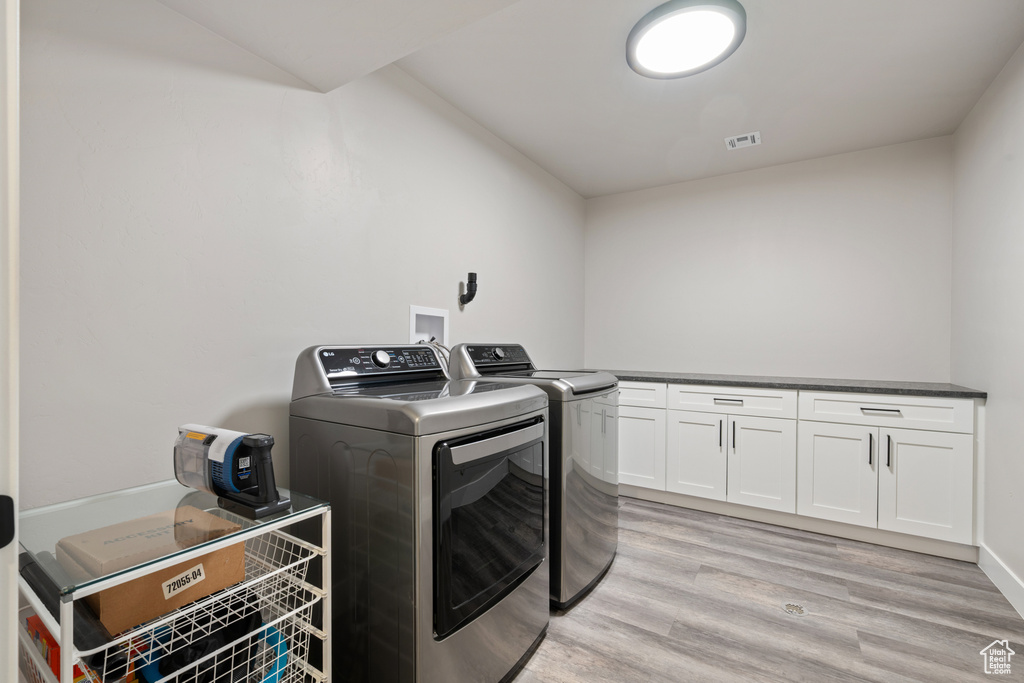 Laundry area with washer and clothes dryer, cabinet space, and light wood-type flooring