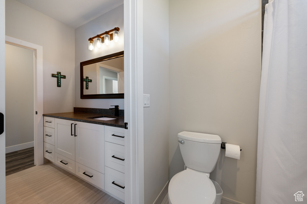 Full bathroom with vanity, toilet, wood finished floors, and baseboards