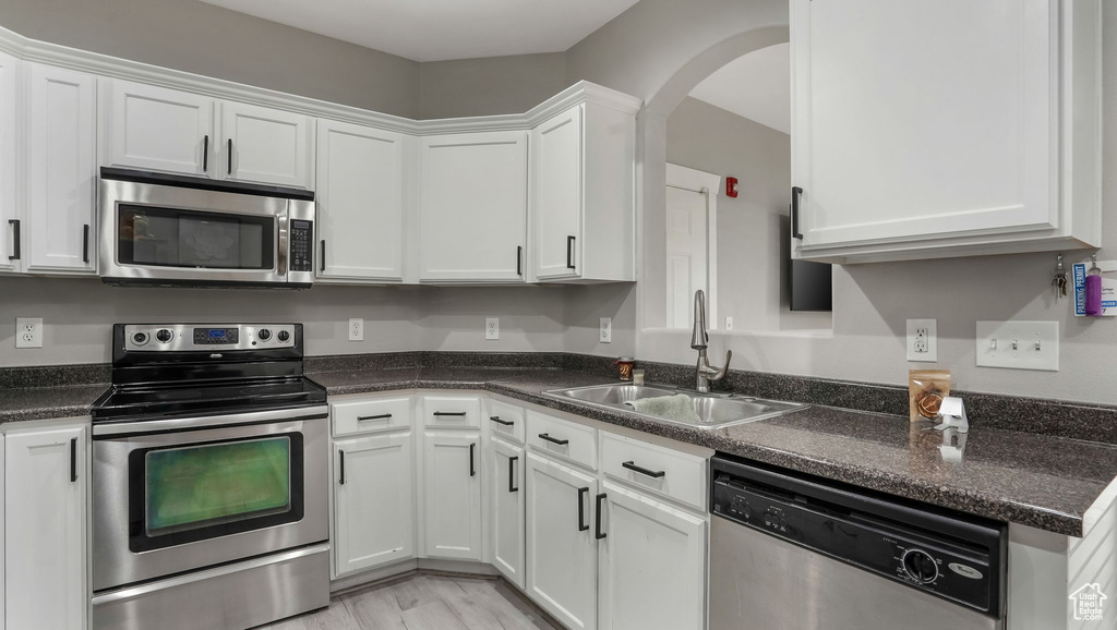 Kitchen with appliances with stainless steel finishes, a sink, white cabinetry, and arched walkways
