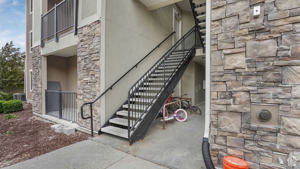 Entrance to property featuring stone siding, central AC, and stucco siding
