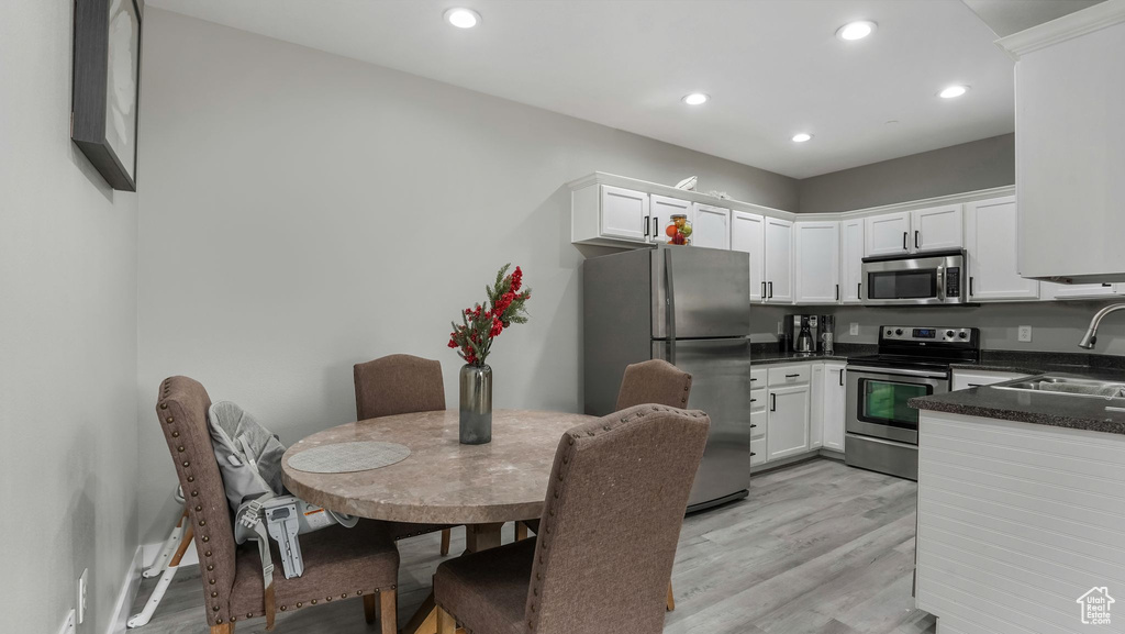 Kitchen with stainless steel appliances, a sink, light wood-style flooring, dark countertops, and white cabinets