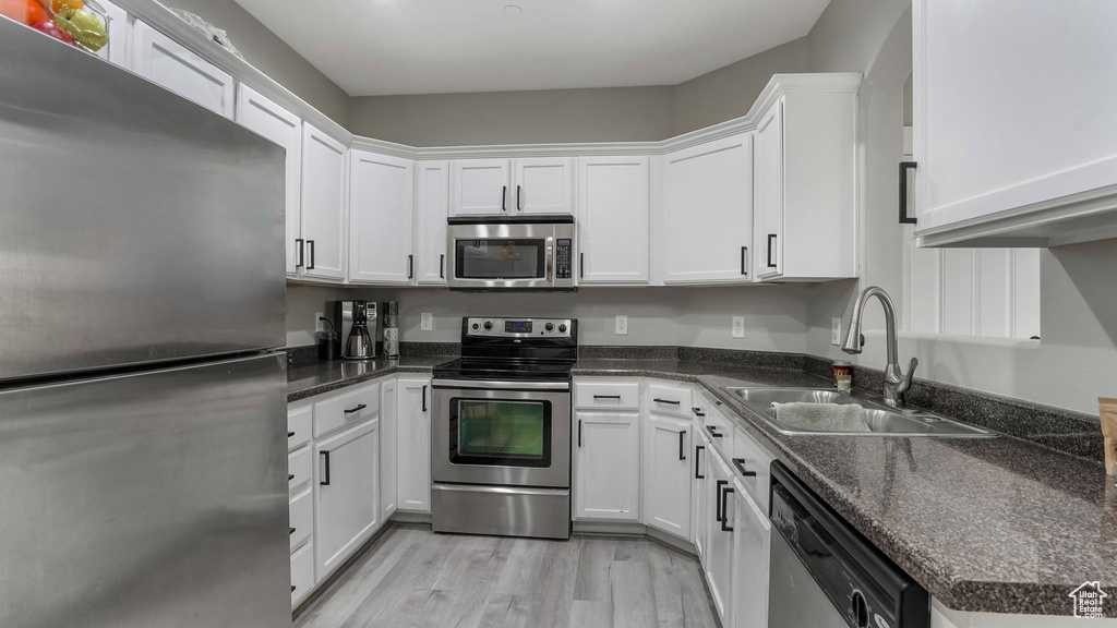 Kitchen with stainless steel appliances, a sink, white cabinetry, and light wood-style flooring