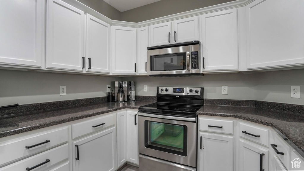 Kitchen featuring appliances with stainless steel finishes, white cabinetry, and dark stone countertops