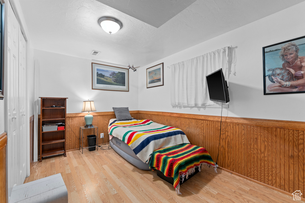 Bedroom with a wainscoted wall, wood finished floors, wooden walls, and a textured ceiling