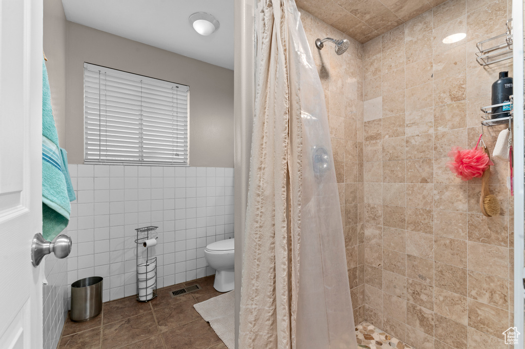 Bathroom featuring tile walls, toilet, a tile shower, and tile patterned flooring
