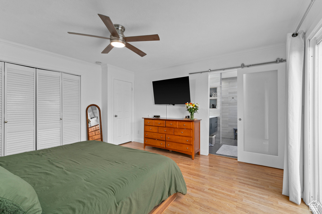 Bedroom featuring ornamental molding, light wood finished floors, a barn door, ensuite bath, and ceiling fan
