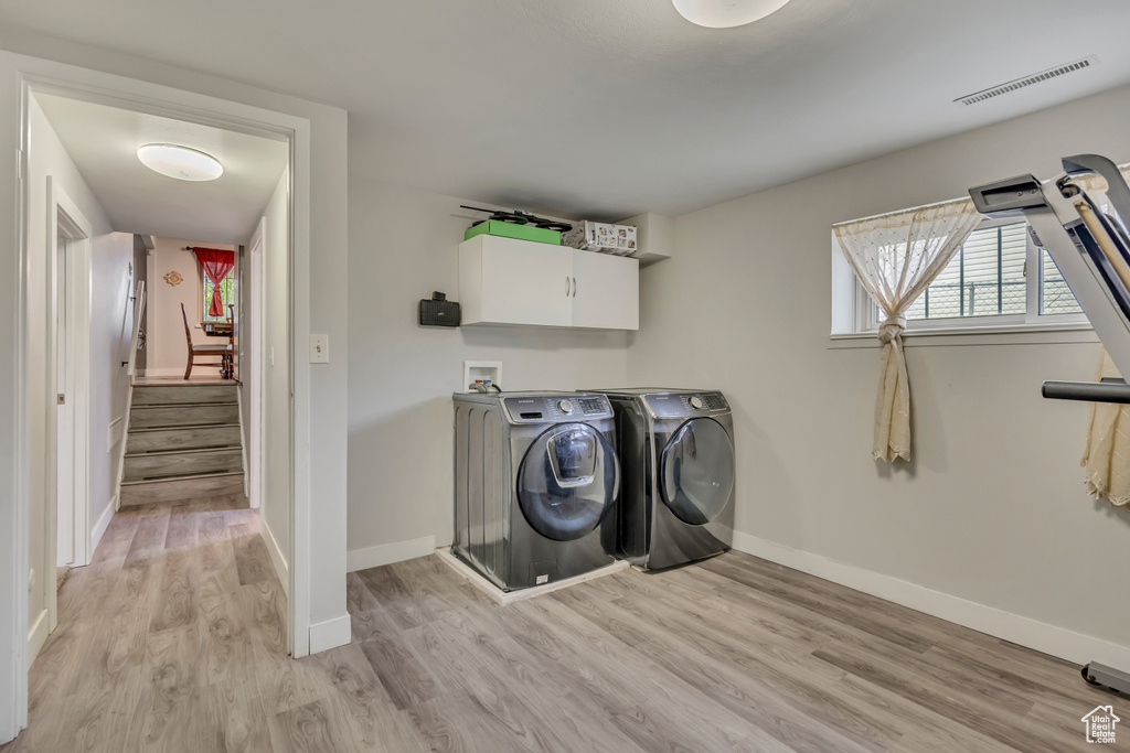 Laundry area with cabinet space, washer and clothes dryer, light wood-style floors, and baseboards