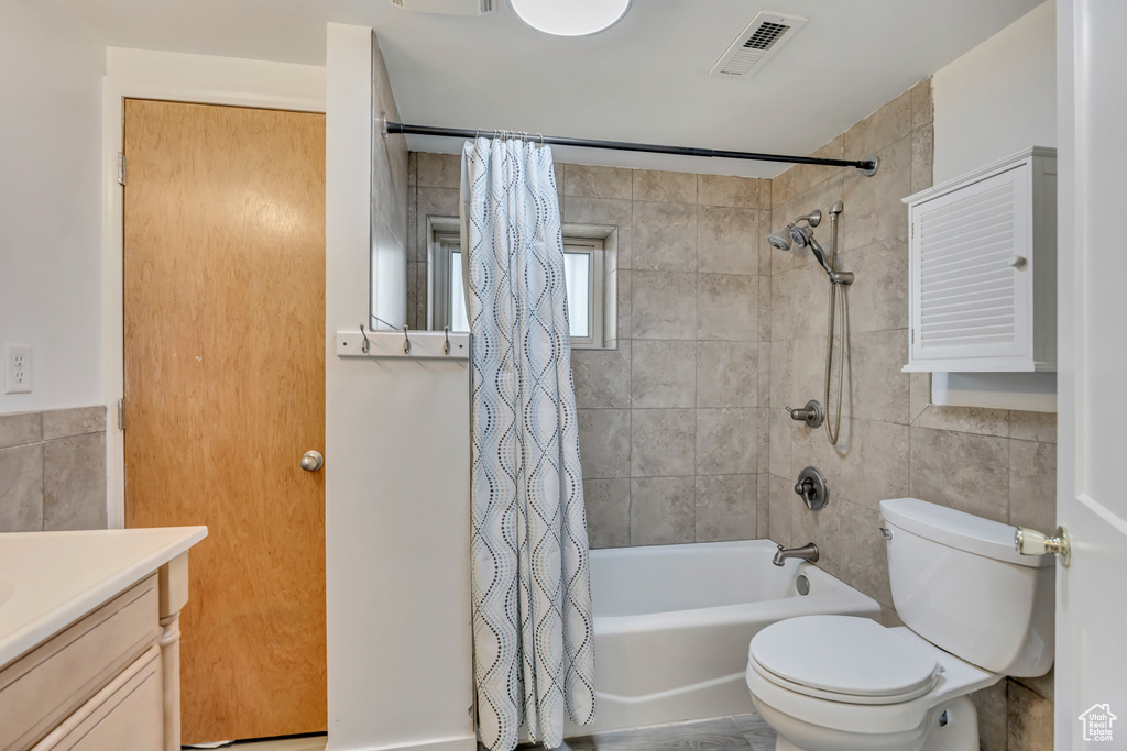 Bathroom featuring tile walls, shower / tub combo with curtain, vanity, and toilet